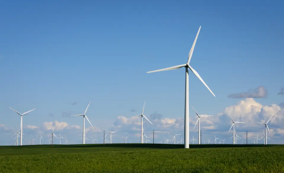 Wind turbines turning over flat green fields under a blue sky