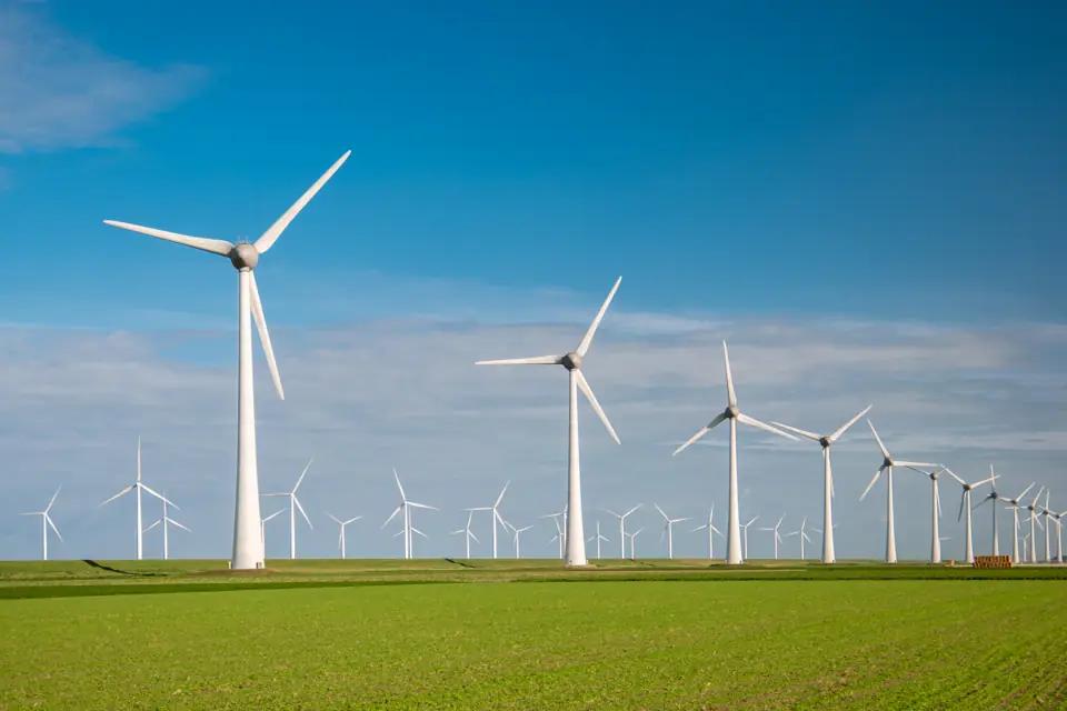 A line of wind turbines across a flat green field